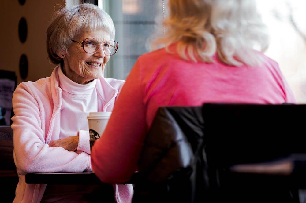 An older woman engaging in social conversation with a younger woman at a coffee shop.